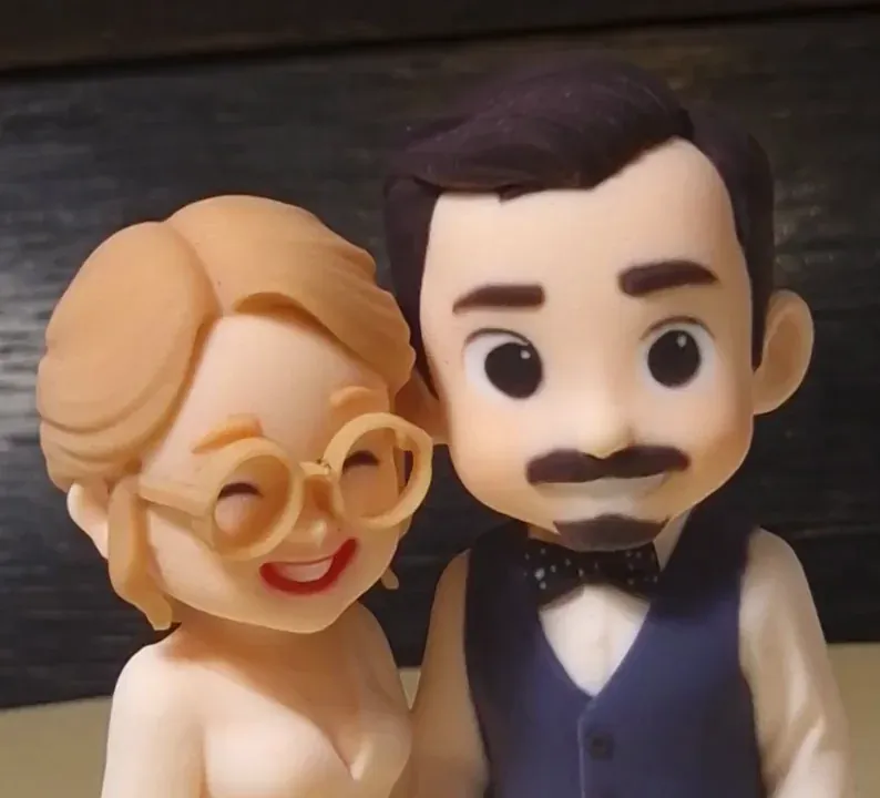 Close-up of a chibi style printed couple with a smooth surface, the bride in round glasses, the groom in a navy vest and dotted bow tie