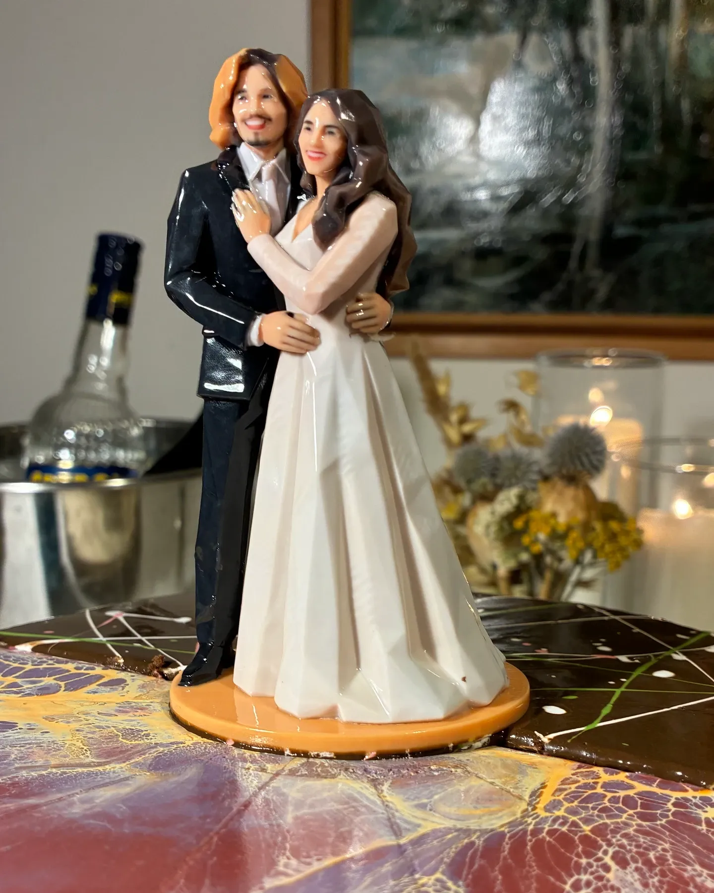 A glossy printed bride and groom on an orange base on a marbled cake, the groom in a black suit, the bride in a white gown