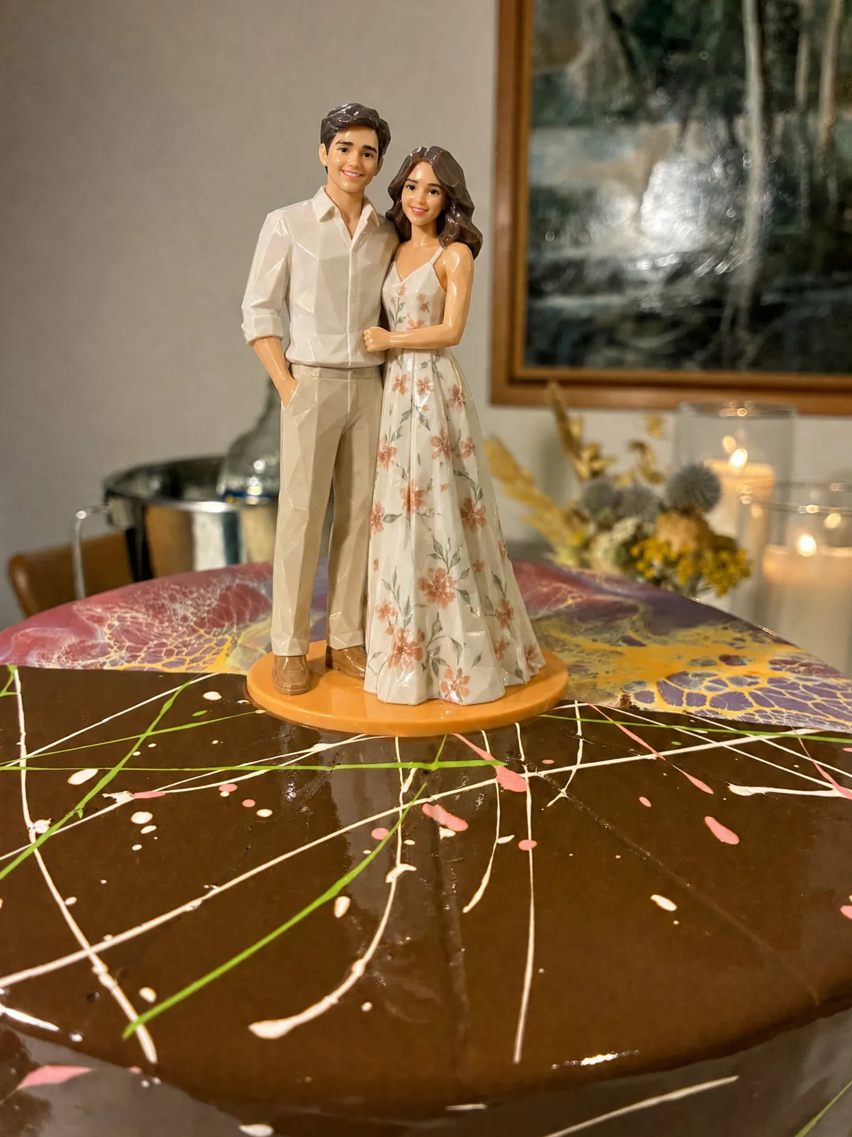 A couple topper on a chocolate cake, he in a linen shirt and beige trousers, she in a long flowered sundress