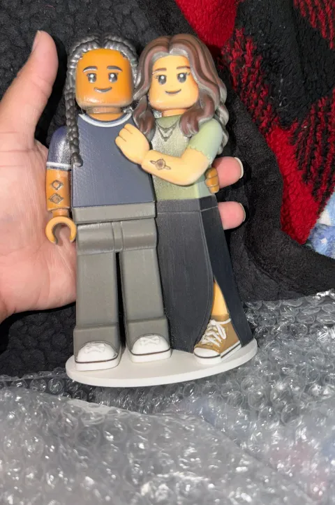 Hand holding a printed figure of two women hugging, on a white round base, above bubble wrap