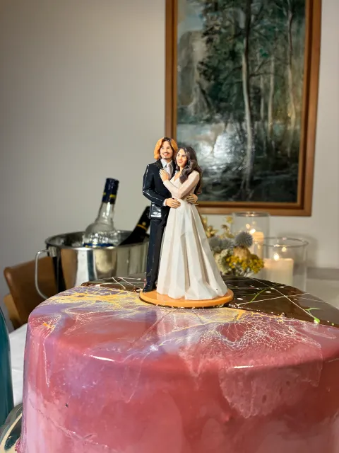 Printed bride and groom figure on an orange base on top of a pink and chocolate glazed cake