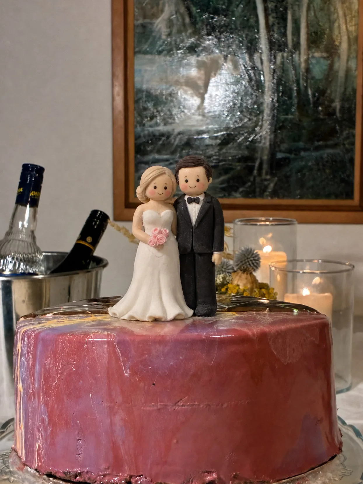 Hand-modelled sugar bride in a white gown and groom in a black jacket with a bow tie, standing on a burgundy glazed cake