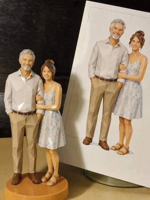A glossy faceted figure of a gray-bearded man in a white shirt and chinos and a young woman in a light blue floral sundress, arm in arm on an orange base, next to a matching drawing on a card.