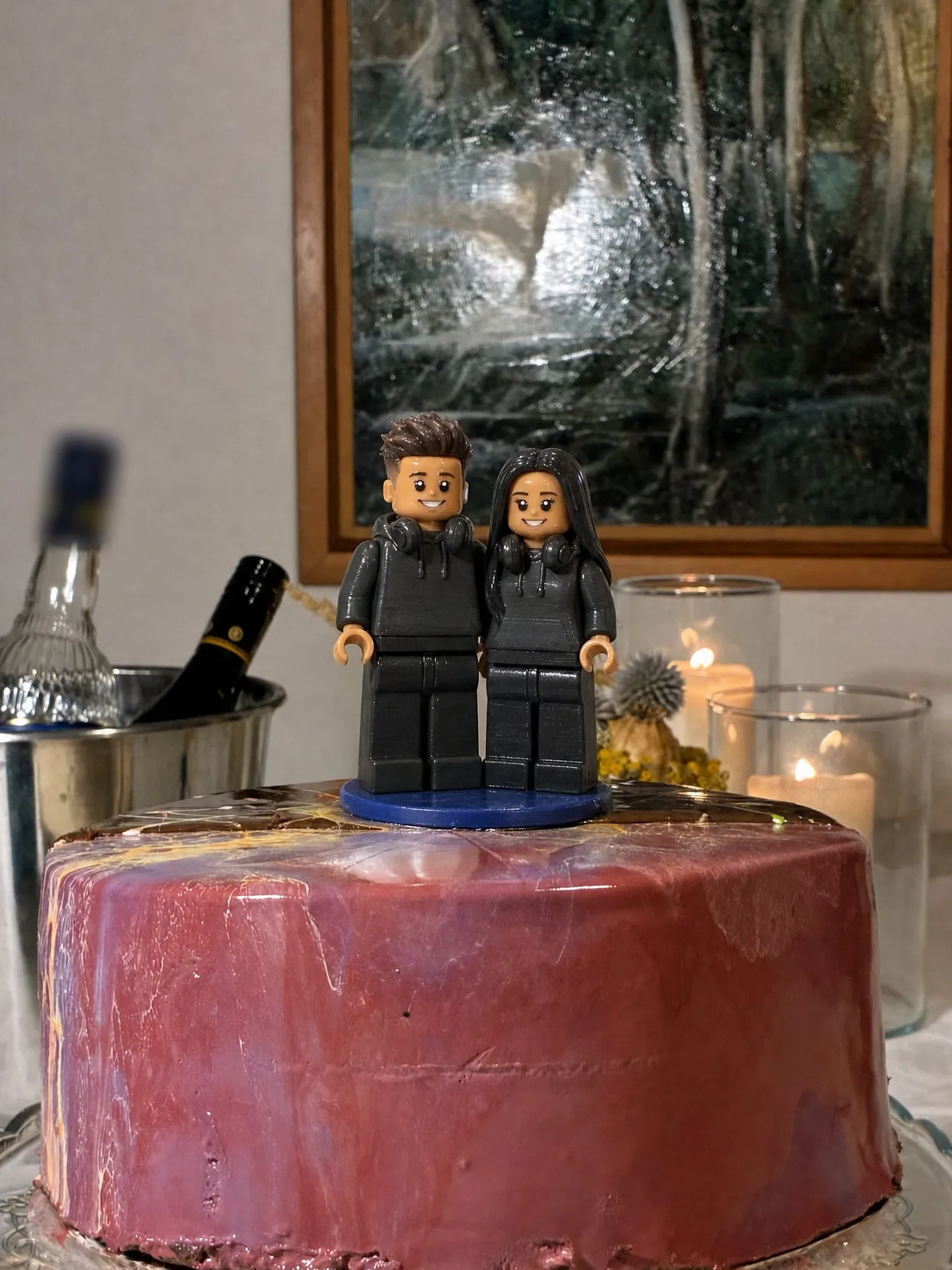 A couple topper in matching hoodies with headphones around their necks, on a pink glazed cake.