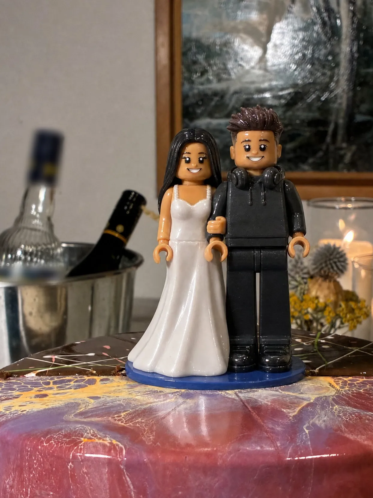 A couple topper, the bride in a white gown and the groom in a dark hoodie with headphones around his neck, on a marbled cake.