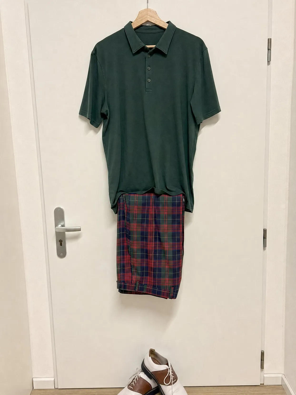 A green polo and red, navy and green tartan trousers on a hanger, saddle shoes below.