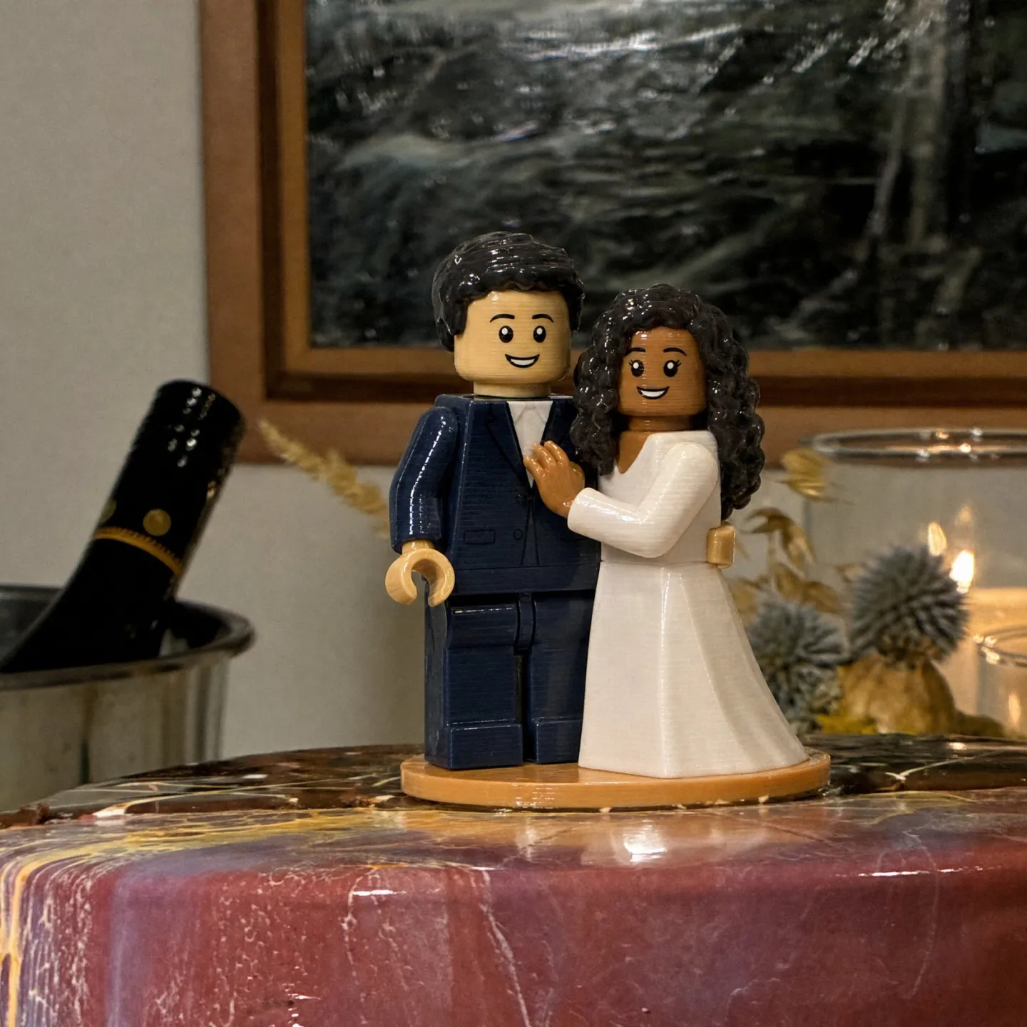 Blocky toy-style topper of a bride with brown skin in a white gown and a groom with light skin in a navy suit.
