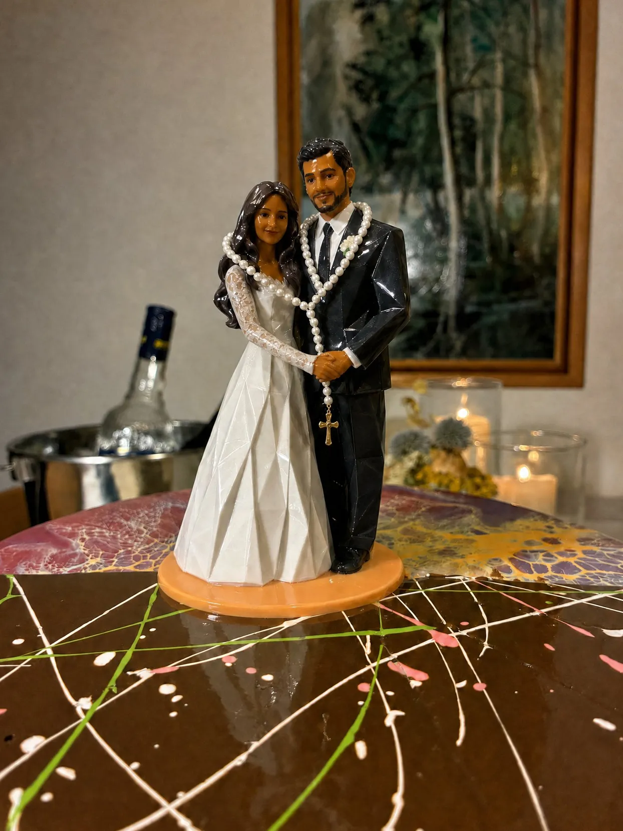 The same couple as a glossy faceted topper on an orange base, a long string of white beads looped over both of them, a small gold cross hanging between them.
