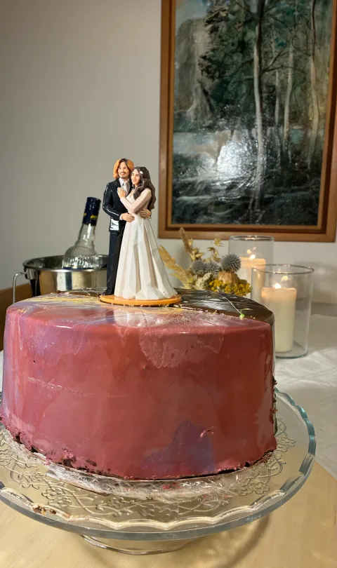 Printed bride and groom figure on a round orange base in the middle of a pink glazed cake on a glass stand