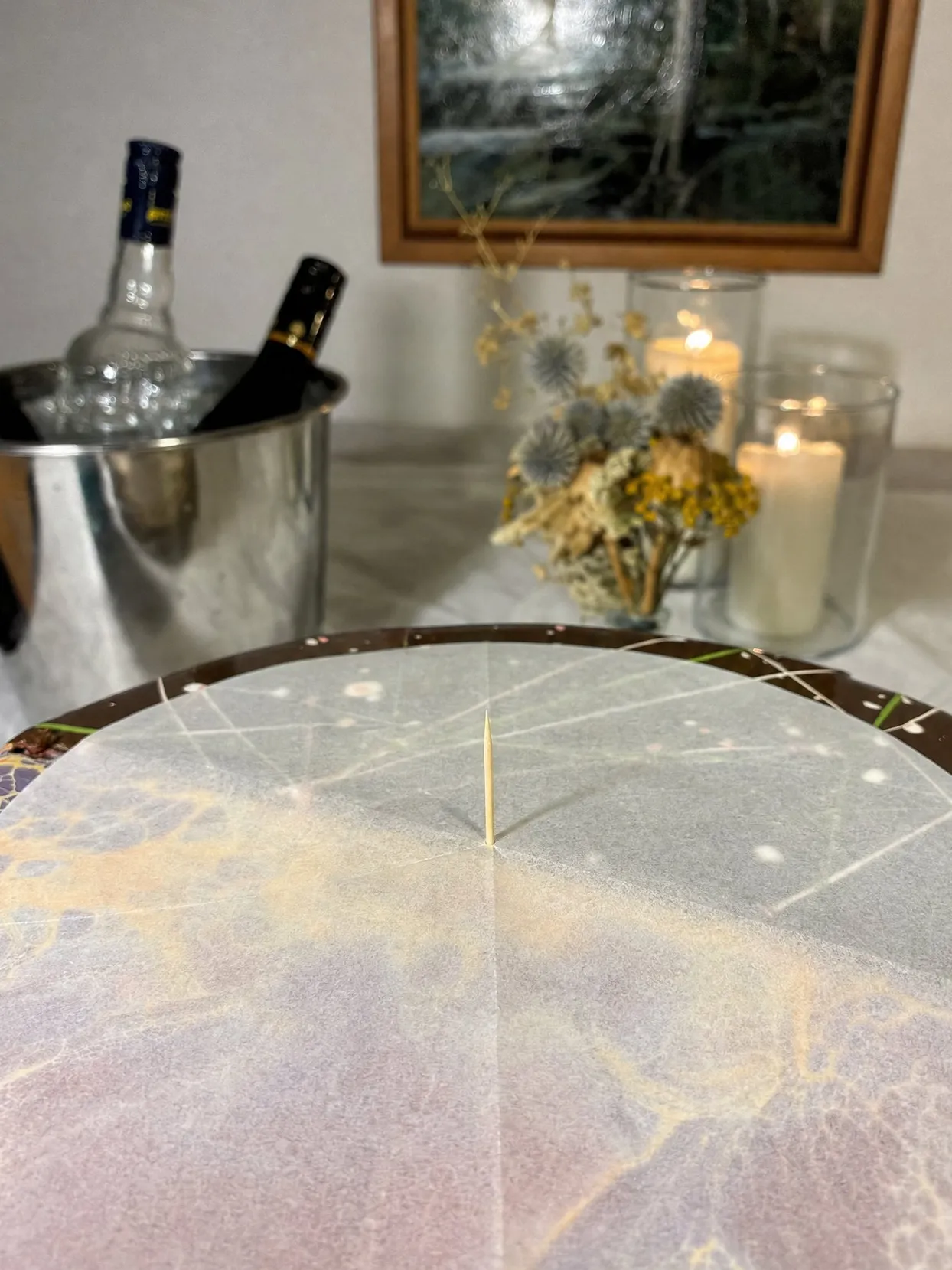 Round sheet of baking paper with 2 crossing fold lines on a cake top, a toothpick standing at the crossing