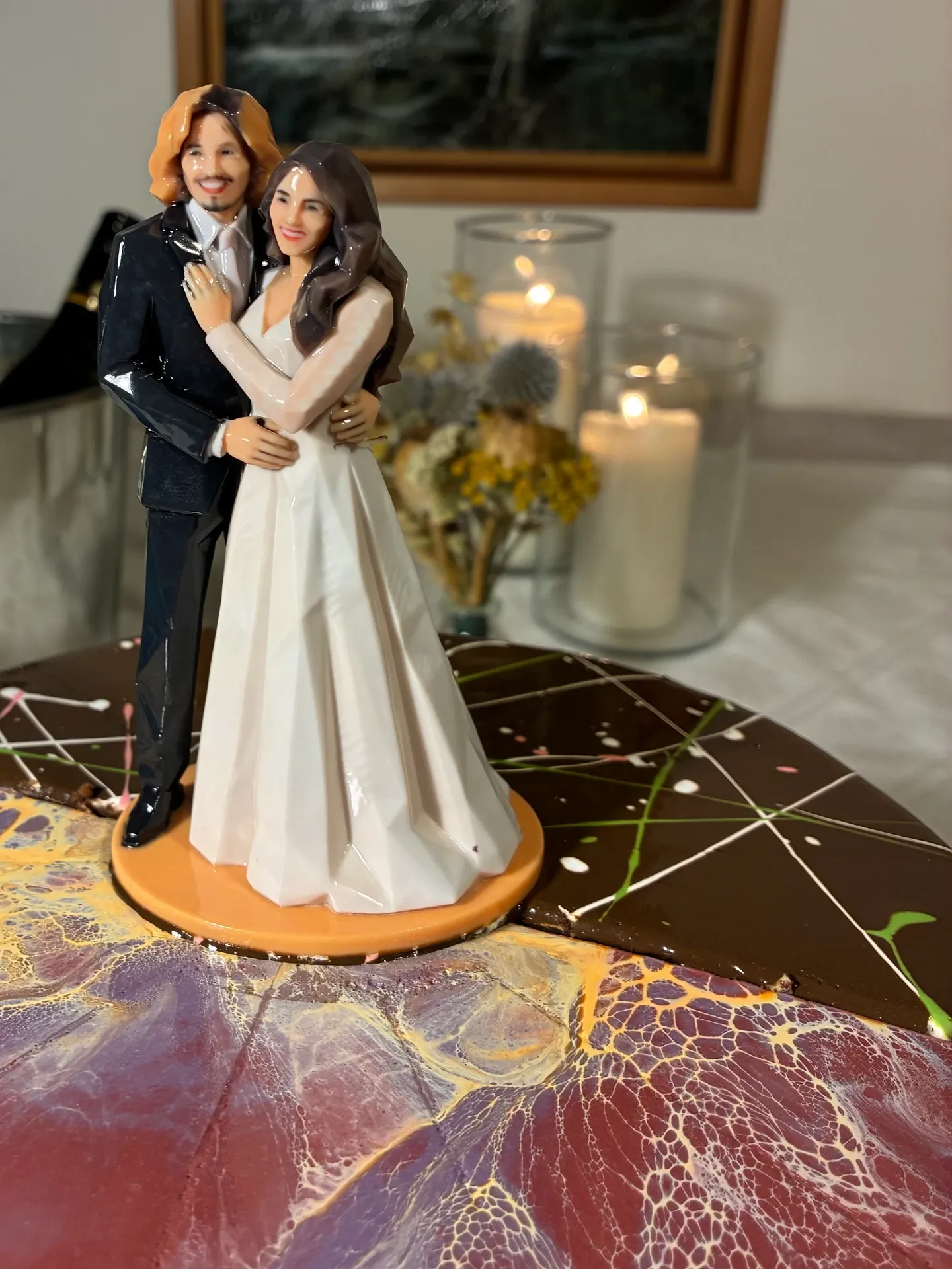 Printed bride and groom figure on an orange base on a cut chocolate and marbled cake, candles behind
