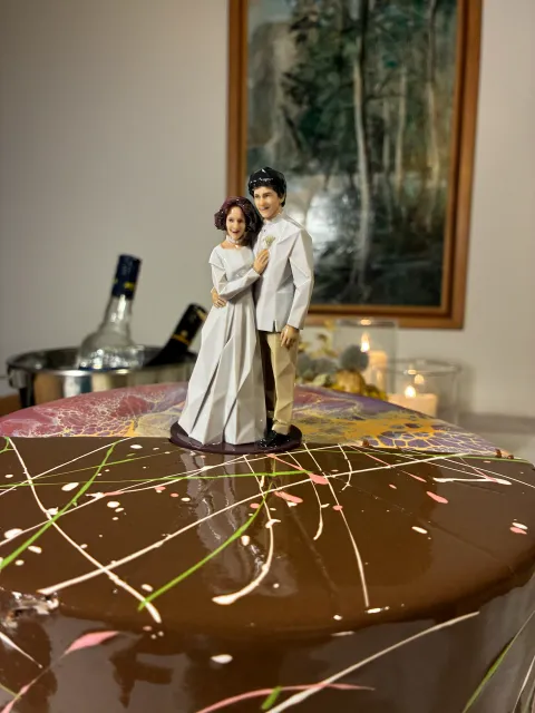 Printed bride and groom figure standing on a small dark base on top of a glazed chocolate cake