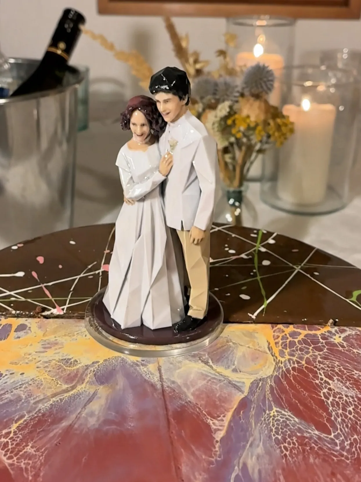 Bride and groom figure standing on a clear round disc on a chocolate and pink marbled cake top
