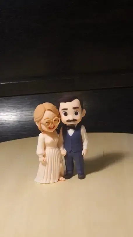 Small clay-style bride and groom figure with round glasses on a wooden turntable