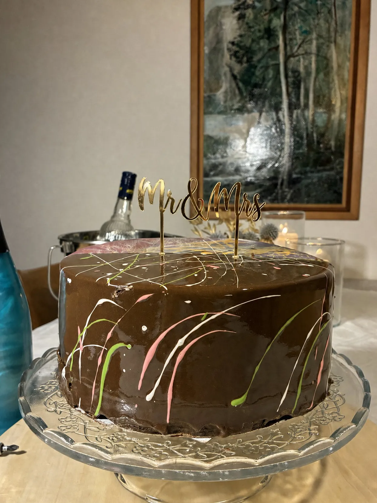 Flat gold mirror acrylic topper reading Mr & Mrs in thin script, standing on two stakes on top of a chocolate glazed cake