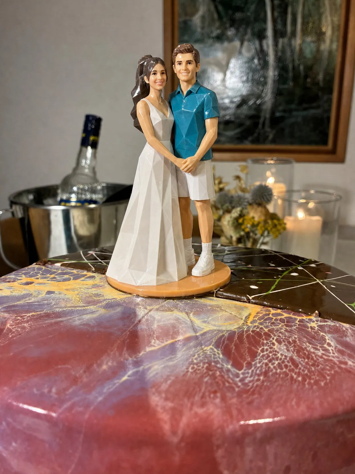 The same topper couple: she in a white A-line gown, he in a teal polo and white shorts, on a marbled cake.