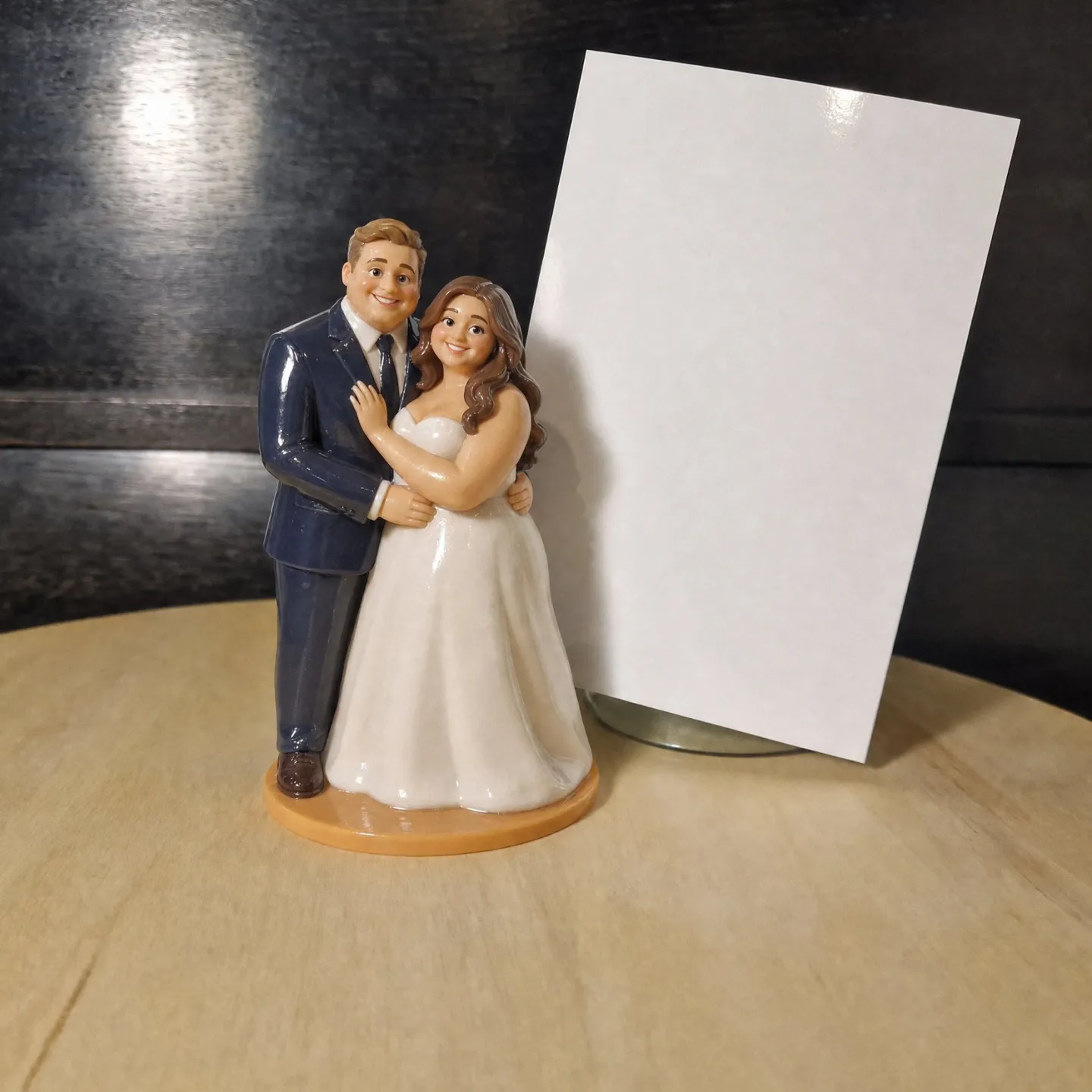 Cake topper figurine of a plus size bride in a strapless white gown and a broad groom in a navy suit, his arm around her waist, on a wooden turntable.