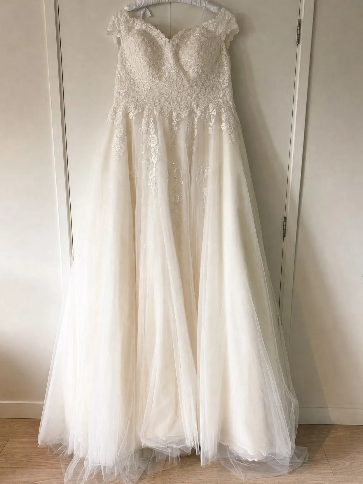 An ivory lace and tulle A-line wedding gown on a padded hanger, hung on a white wardrobe door.
