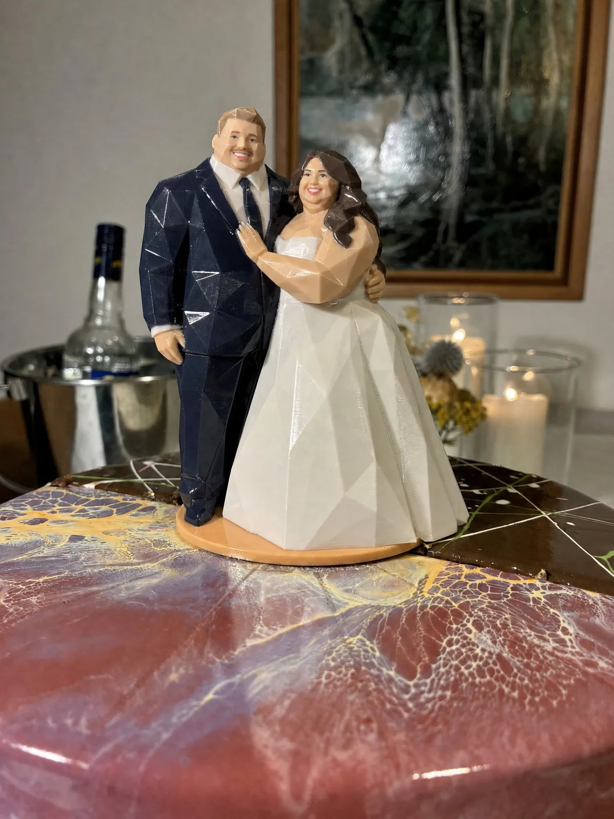 Origami style cake topper of a plus size bride in a white gown and a groom in a navy suit, on a round base on a marbled pink cake.