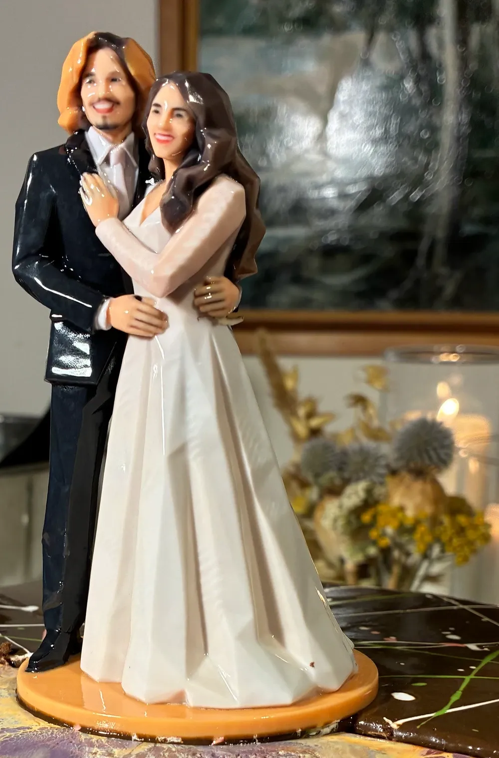 Close view of a glossy printed couple in an embrace on a round orange base, the groom in a dark suit and the bride in a pale gown