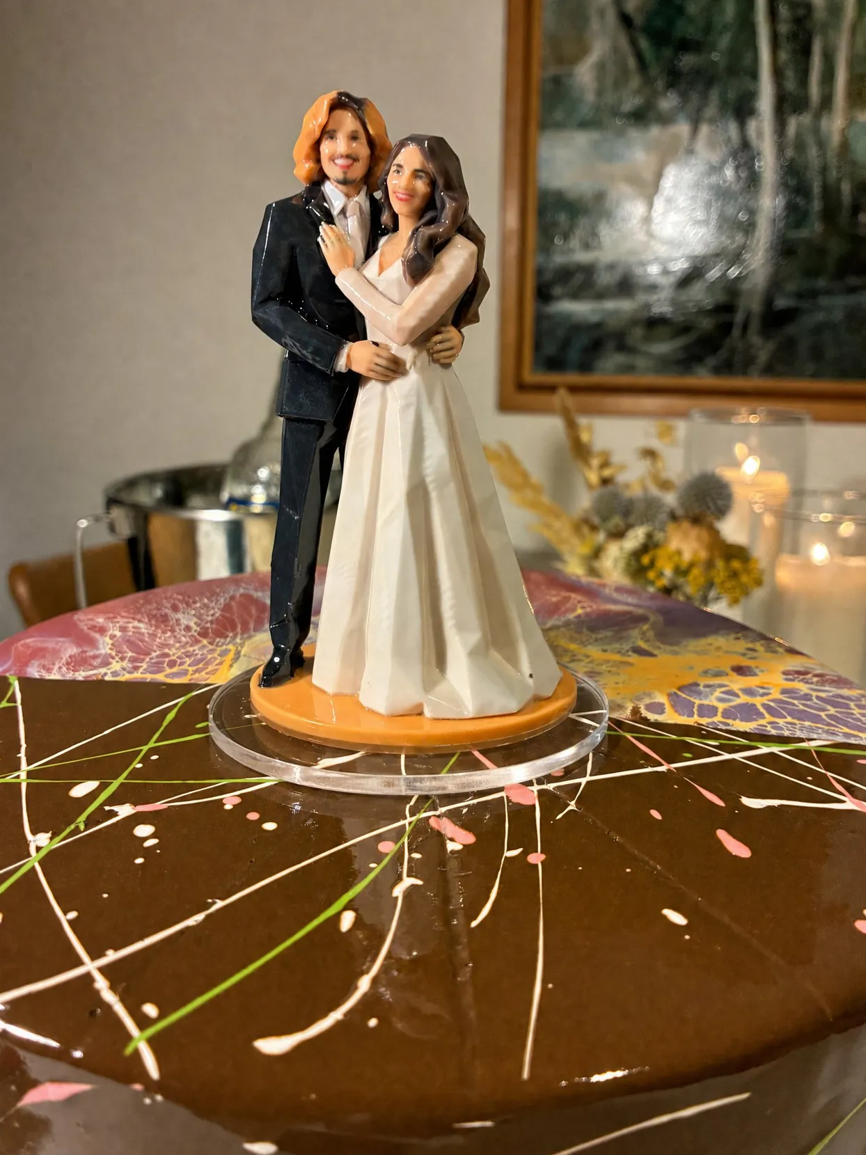 Bride and groom figure on an orange base standing on a clear round disc on a chocolate drip cake top