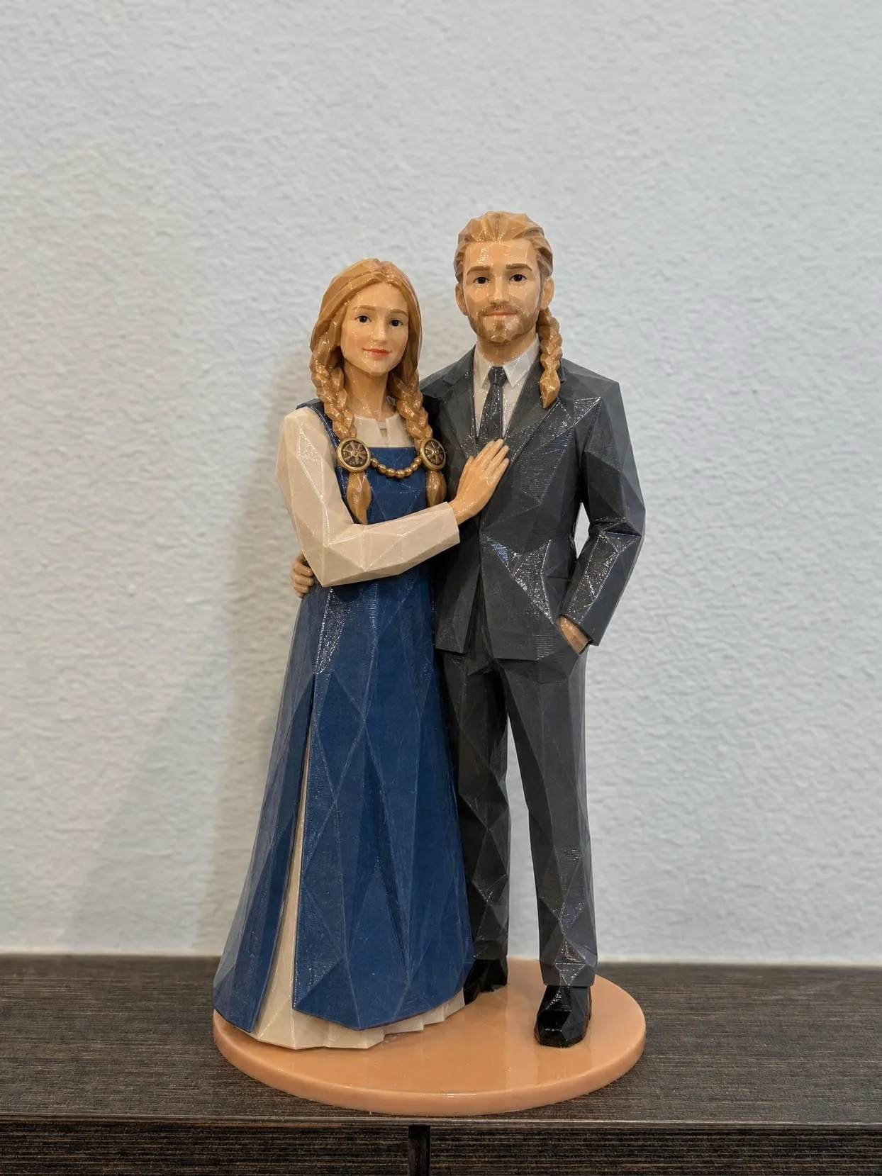 A couple topper on a shelf, the bride in a blue apron dress with bronze brooches and braids, the groom in a gray suit and tie
