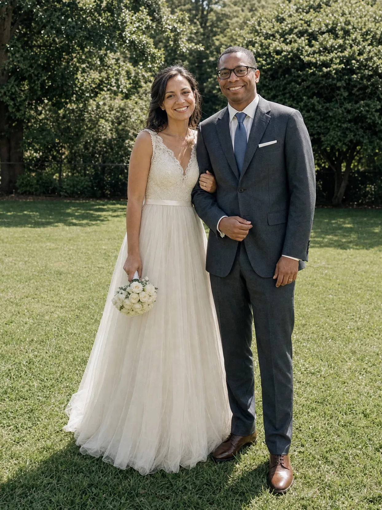 Dasselbe Paar an seinem Hochzeitstag auf einem Rasen, sie im elfenbeinfarbenen Kleid, er im anthrazitfarbenen Anzug.
