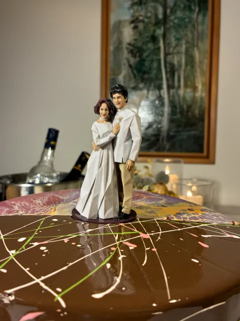 Printed Origami couple in white standing close on a chocolate cake.
