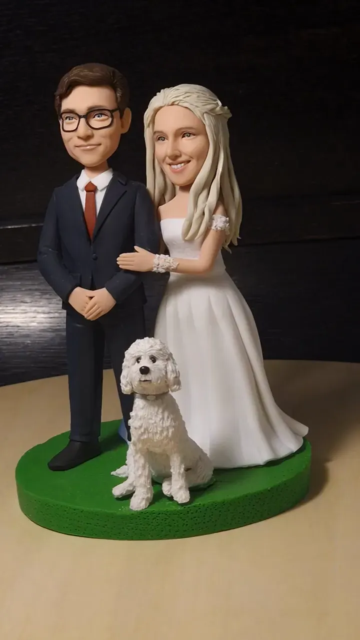 Clay figure of a groom in glasses and a bride in white with a small white dog, on a green base