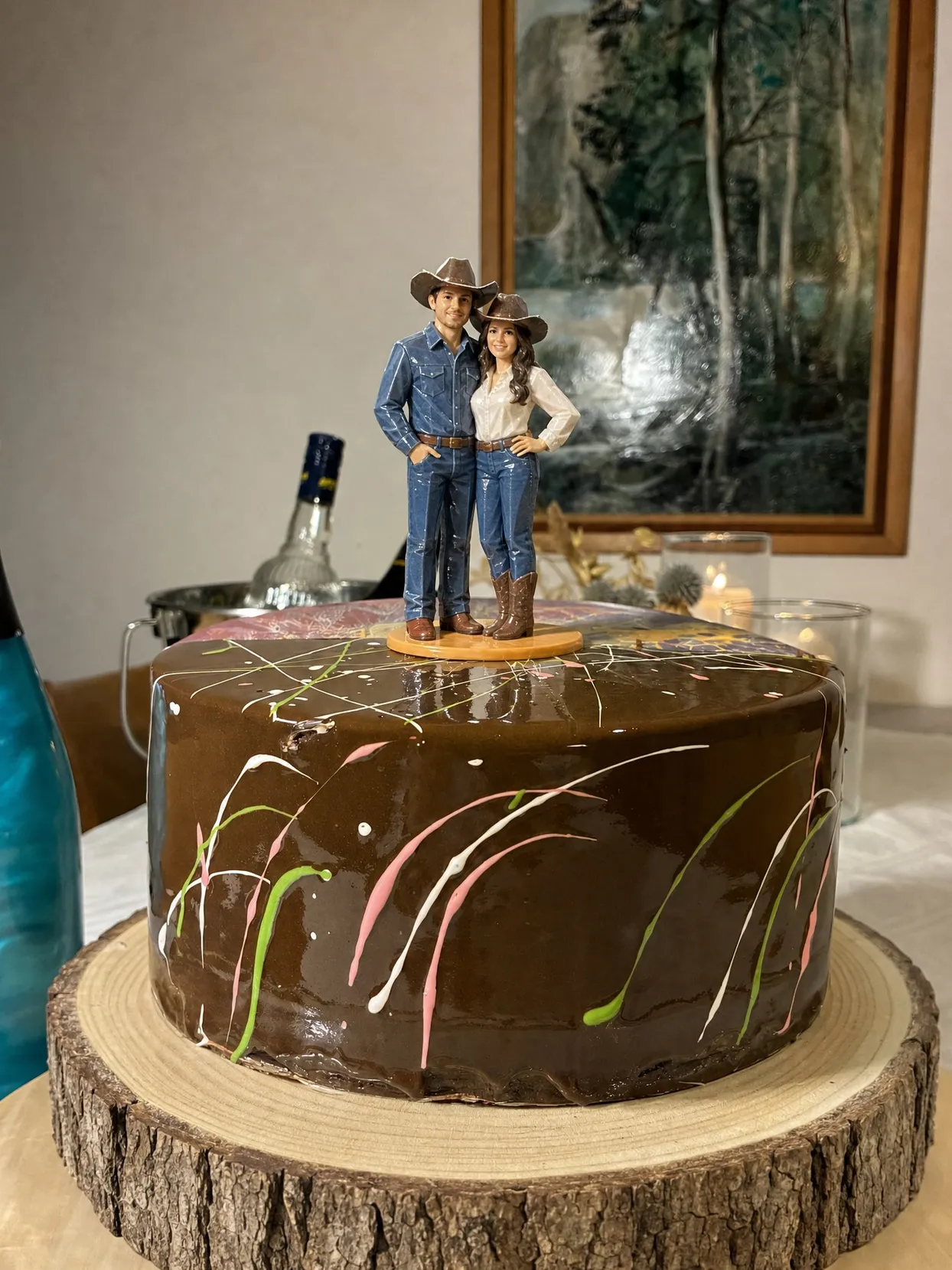 A couple topper in cowboy hats, jeans and boots on a chocolate cake on a wood slice stand.