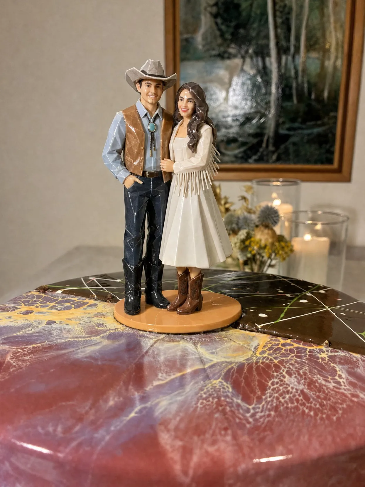 A couple topper, the groom in a gray cowboy hat, brown leather vest and bolo tie, the bride in an ivory fringed dress and brown boots, on a pink marbled cake