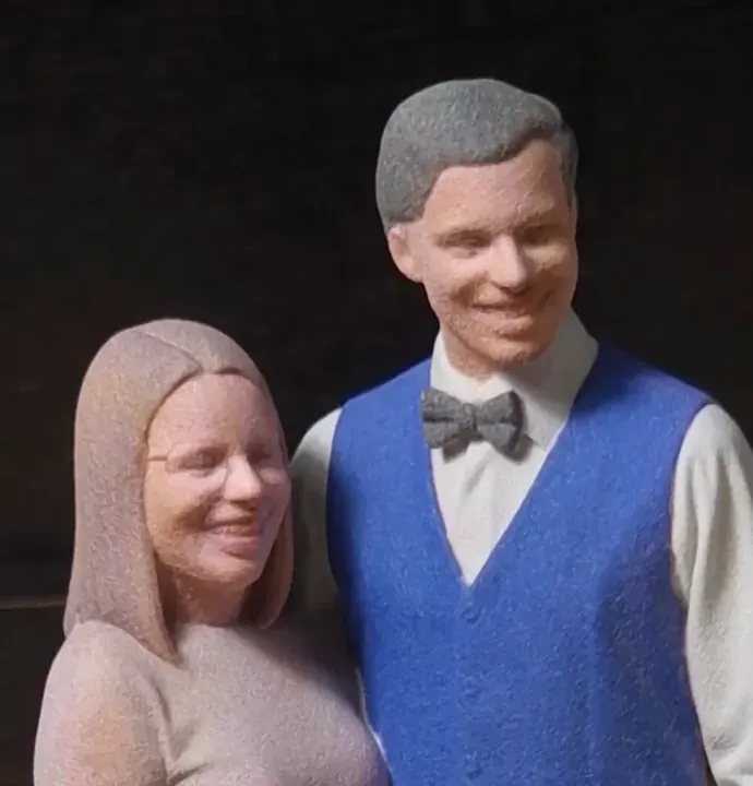 Close-up of a printed couple's faces with a speckled grainy surface, the man in a blue vest and grey bow tie